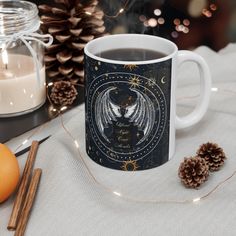 a coffee mug with an angel on it next to some cinnamons and pine cones