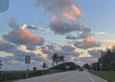 the sun is setting on an empty road with palm trees in the foreground and clouds in the background