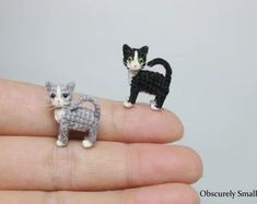 two tiny crocheted cats are sitting on someone's finger, one is black and the other is white