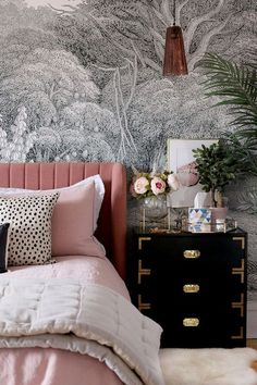 a bed with pink sheets and pillows in front of a wallpapered forest scene