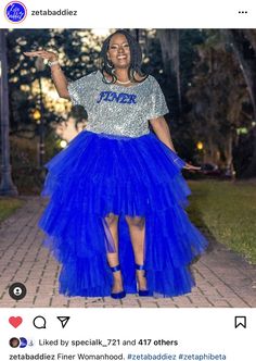 a woman in a blue skirt and t - shirt is standing on the sidewalk with her hand up