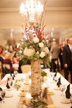 a vase with flowers and greenery on a table in a room filled with people