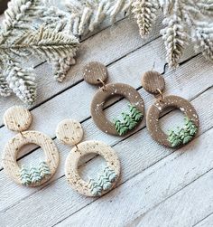 three pairs of earrings sitting on top of a wooden table next to pine cones and branches