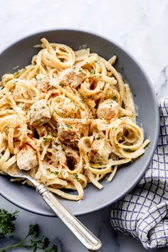 a bowl full of pasta with meatballs and parsley on the side next to a fork