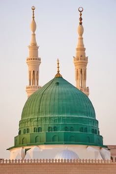 a green dome on top of a building with two minalis in the background,