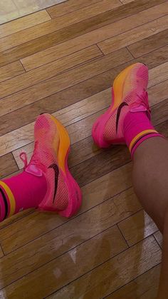 a woman's feet in pink and yellow shoes on the floor with wood floors