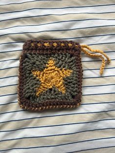 a crocheted square with a yellow star on it sitting on top of a striped shirt