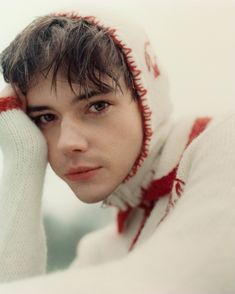 a young man wearing a white and red sweater holding his hand to his face while looking at the camera