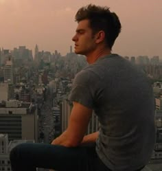 a man sitting on top of a tall building looking out over the cityscape