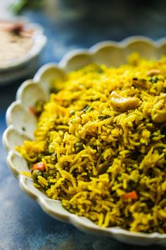 a white bowl filled with yellow rice on top of a blue tablecloth next to other dishes