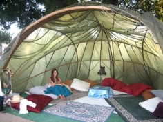 a woman sitting in a tent on top of a green floor covered with blankets and pillows