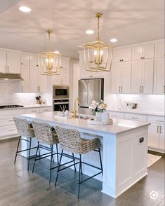 a large kitchen with white cabinets and an island in the middle is lit by pendant lights