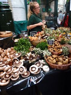 a woman standing in front of a table filled with lots of mushrooms and other vegetables