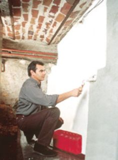 a man is painting the wall with white paint and red buckets in front of him