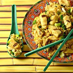 a plate with rice and chicken on it next to two spoons that have chopsticks in them