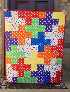 a multicolored patchwork quilt is hanging on a door mat in front of a brick wall