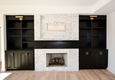 an empty living room with black cabinets and a white brick fireplace in the center surrounded by wood flooring