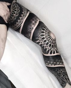 a man is sitting on a bed with his leg covered in black and white tattoos