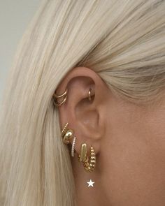 a woman with blonde hair wearing three gold ear cuffs and two small white stars on the back of her ear