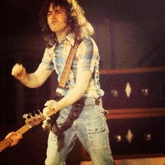 a man with long hair holding a guitar in his hand while standing on a stage