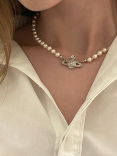 a woman wearing a white shirt and pearl necklace with a crown on it's collar