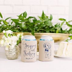 two personalized can coolers sitting on a table with flowers and cake in the background