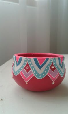 a pink and blue bowl sitting on top of a white table next to a window