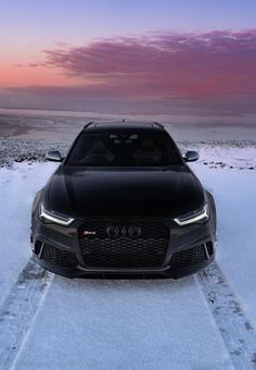 the front end of a black car parked on snow covered ground with sunset in background