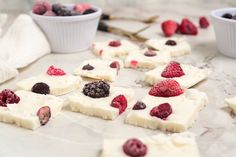 some desserts are arranged on a table with berries and other toppings around them