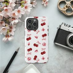 an iphone case with cherries on it next to a camera and some pink flowers