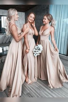 three beautiful women standing next to each other in long dresses and one is holding a bouquet