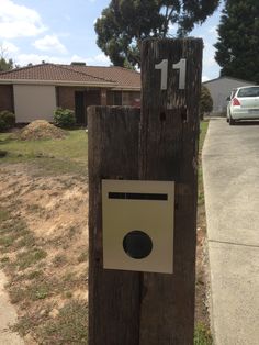 a wooden post with a sign attached to it in front of a house and car