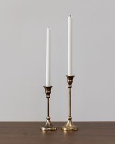 two white candles sitting on top of a table next to each other with one candle in the middle