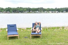 a woman laying on top of a blue lawn chair next to a lake