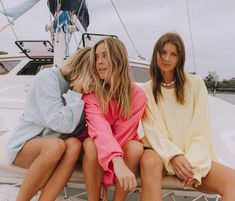 three young women sitting on the back of a boat in front of a sailboat