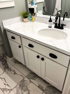 a bathroom with marble counter tops and white cabinets, along with black faucets