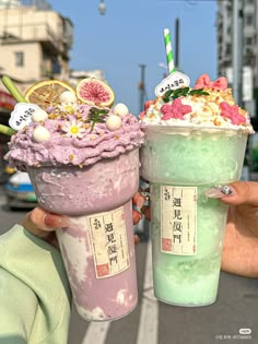 two ice cream sundaes are being held up in front of each other on the street