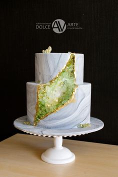 a marbled cake with green and gold decorations on a white pedestal in front of a black wall