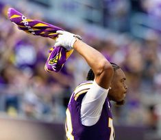 a football player holding his arm up in the air while wearing a purple and yellow uniform