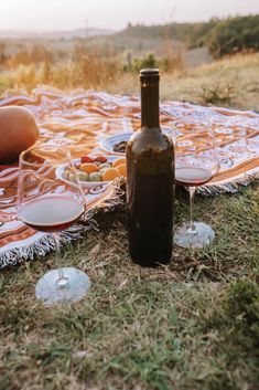 a bottle of wine sitting on top of a blanket next to some glasses and food