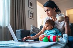 a woman holding a baby while using a laptop