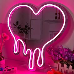 a pink heart shaped neon sign sitting on top of a table next to a mirror