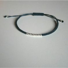 a blue string bracelet with silver beads on a white surface, the bead is attached to an adjustable cord