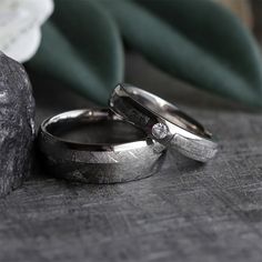 two wedding rings sitting next to each other on top of a wooden table in front of a rock