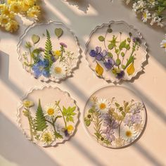 four plates with pressed flowers on them sitting on a table next to yellow and white flowers