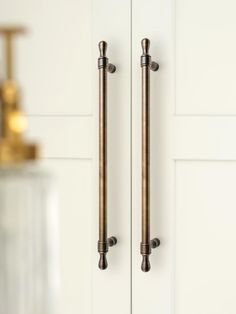 two brass handles on the front door of a white kitchen with gold faucet and soap dispenser