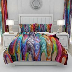 a bed with colorful comforters and pillows on it in a room that has white furniture