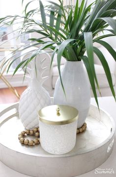 two white vases sitting on top of a table next to a potted plant