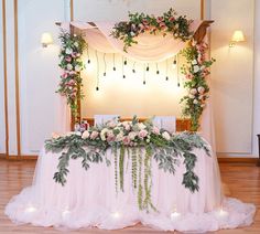 a table with flowers and greenery is set up for a wedding reception in the middle of a room