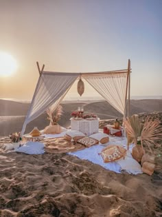 an outdoor desert wedding setup with white draping and food on the sand at sunset